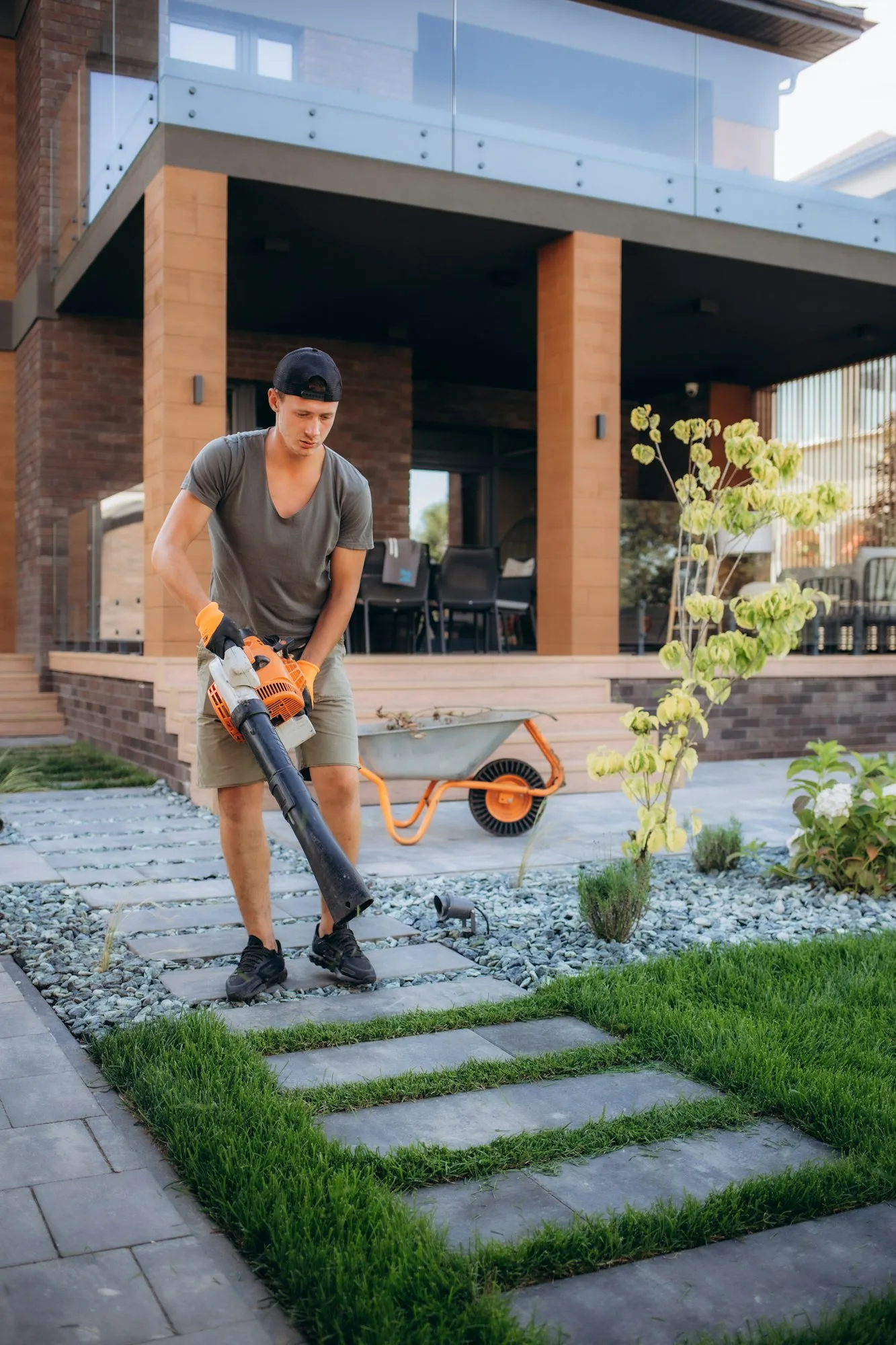 Professional Gardener with Leaf Blower in His Hand Cleaning Residential Backyard Garden.